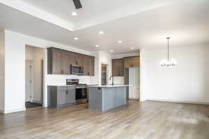 Kitchen with stainless steel appliances, hanging light fixtures, light countertops, and a kitchen island with sink