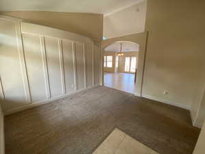 Unfurnished room with arched walkways, high vaulted ceiling, light tile patterned flooring, light colored carpet, and baseboards