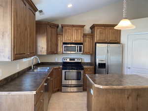 Kitchen featuring dark countertops, appliances with stainless steel finishes, vaulted ceiling, and a sink