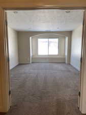 Empty room featuring a textured ceiling, carpet, and baseboards