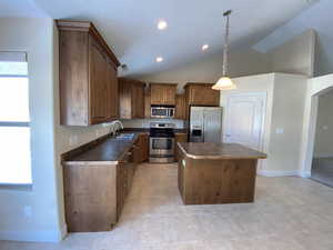 Kitchen featuring a sink, appliances with stainless steel finishes, a center island, dark countertops, and decorative light fixtures