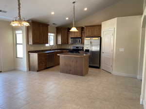 Kitchen featuring appliances with stainless steel finishes, dark countertops, decorative light fixtures, and a kitchen island