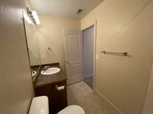 Half bath with toilet, baseboards, visible vents, and vanity