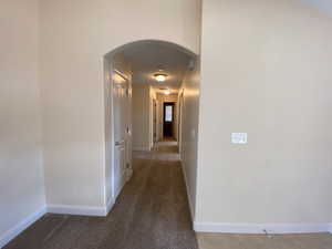 Hallway featuring arched walkways, dark carpet, and baseboards