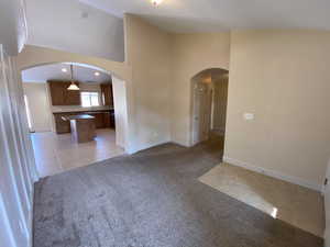 Unfurnished living room with arched walkways, light tile patterned floors, light carpet, high vaulted ceiling, and baseboards