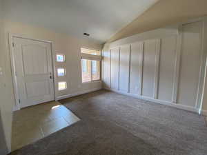 Tiled entrance foyer with carpet flooring, vaulted ceiling, and visible vents