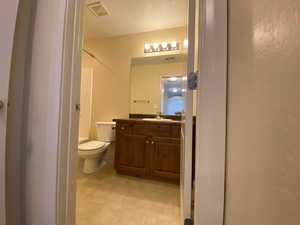 Full bathroom with visible vents, a textured wall, toilet, tile patterned floors, and vanity