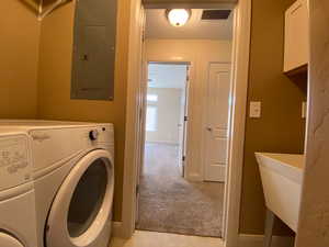 Clothes washing area featuring light colored carpet, visible vents, a sink, washer and dryer, and electric panel