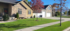 View of front of property with roof with shingles, stucco siding, a front yard, stone siding, and driveway