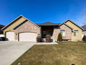 View of front of house with stucco siding, concrete driveway, an attached garage, a front yard, and stone siding