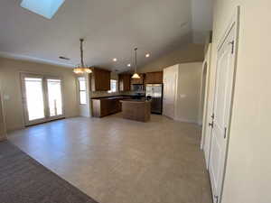 Kitchen featuring stainless steel appliances, open floor plan, hanging light fixtures, a center island, and lofted ceiling with skylight