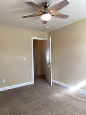 Carpeted empty room with a textured ceiling, baseboards, and a ceiling fan