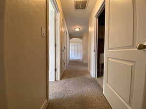 Corridor with arched walkways, visible vents, a textured wall, light carpet, and baseboards