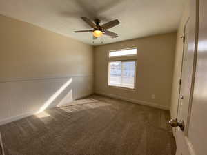 Empty room with a wainscoted wall, a ceiling fan, and carpet flooring