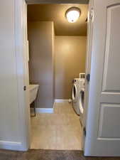 Laundry area with laundry area, light tile patterned floors, baseboards, a textured ceiling, and washing machine and dryer