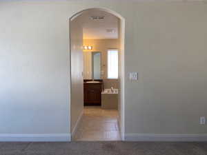 Hall with arched walkways, light tile patterned floors, light colored carpet, visible vents, and a sink