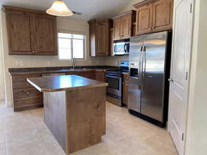 Kitchen featuring a sink, appliances with stainless steel finishes, a center island, dark countertops, and decorative light fixtures