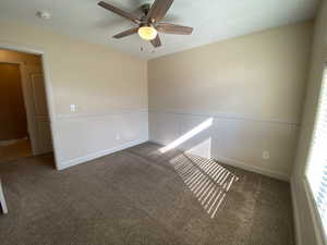 Unfurnished room featuring ceiling fan, dark colored carpet, and wainscoting