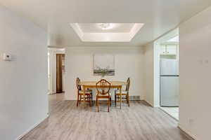 Dining space with a tray ceiling, light wood-type flooring, visible vents, and baseboards