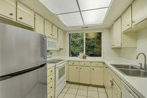 Kitchen with light tile patterned floors, cream cabinets, white appliances, a sink, and light countertops