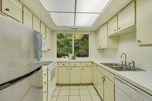 Kitchen with light countertops, white appliances, a sink, and cream cabinetry