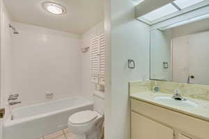 Full bathroom with a skylight, toilet, tile patterned flooring, vanity, and shower / washtub combination