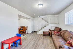 Living area with a textured ceiling, visible vents, baseboards, stairway, and light wood finished floors