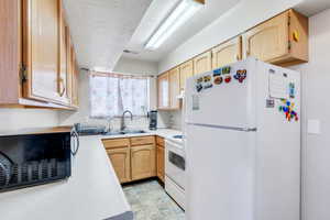 Kitchen with a textured ceiling, under cabinet range hood, white appliances, a sink, and light countertops