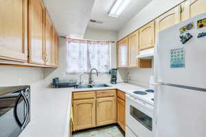 Kitchen with visible vents, light countertops, a sink, white appliances, and under cabinet range hood