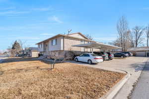 View of side of home with covered and uncovered parking, a yard, and brick siding