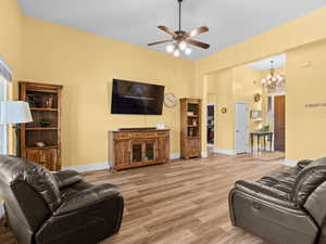 Living room featuring ceiling fan with notable chandelier, light wood-style flooring, and baseboards