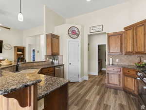 Kitchen with stainless steel appliances, brown cabinets, tasteful backsplash, dark stone counters, and light wood finished floors