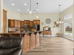 Kitchen with appliances with stainless steel finishes, a towering ceiling, a breakfast bar area, light wood-style floors, and dark stone counters