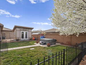 View of yard featuring a patio, a fenced backyard, french doors, an outdoor structure, and a hot tub