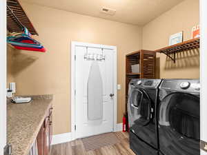 Laundry room with light wood finished floors, visible vents, baseboards, washing machine and dryer, and a textured ceiling