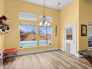 Dining room featuring visible vents, wood finished floors, a high ceiling, an inviting chandelier, and baseboards