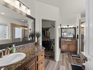 Full bath with a shower stall, wood finished floors, two vanities, and a sink