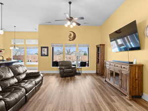 Living room with visible vents, baseboards, wood finished floors, and ceiling fan with notable chandelier