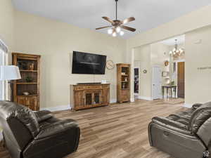 Living room with ceiling fan, a chandelier, light wood finished floors, and a high ceiling