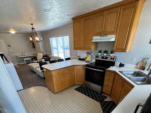 Kitchen with a peninsula, light countertops, decorative light fixtures, and stainless steel range with electric cooktop