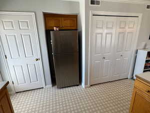 Kitchen with freestanding refrigerator, brown cabinets, and visible vents