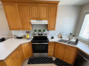 Kitchen with brown cabinets, stainless steel appliances, light countertops, a sink, and under cabinet range hood