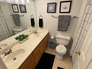 Full bathroom with double vanity, a sink, toilet, and baseboards