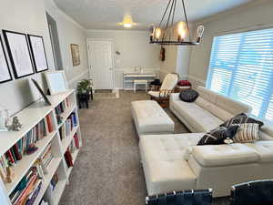 Carpeted living area featuring a chandelier, crown molding, and a textured ceiling