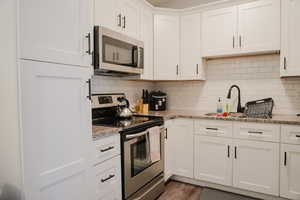 Kitchen featuring stainless steel appliances, decorative backsplash, light stone countertops, and white cabinets