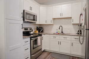 Kitchen with appliances with stainless steel finishes, white cabinets, and light stone countertops