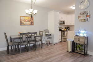 Kitchen with tasteful backsplash, white cabinets, appliances with stainless steel finishes, hanging light fixtures, and light countertops