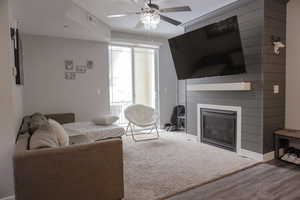 Living room with ceiling fan, wood finished floors, visible vents, baseboards, and a glass covered fireplace