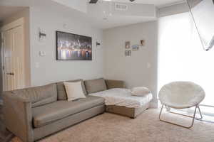 Living room with light carpet, visible vents, and a ceiling fan