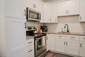 Kitchen featuring a sink, white cabinetry, appliances with stainless steel finishes, light stone countertops, and tasteful backsplash